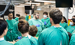 Studenten in stehen in grüner Kleidung um einen Sektionstisch.