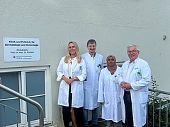 Vier Personen in weißen Kitteln stehen vor einer hellen Wand neben einem Schild der Klinik und Poliklinik für Dermatologie und Venerologie