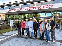 Gruppe von neun Personen steht vor dem Gebäude der Universitätsmedizin Rostock, eine Person trägt einen weißen Arztkittel