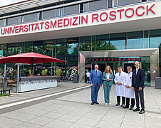 Eine Personengruppe steht vor dem Haupteingang der Unimedizin Rostock