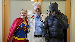 Ein Arzt steht zwischen einem Supergirl und einem Batman