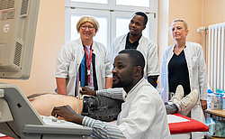 Zwei Rostocker Ärztinnen und medizinisches Personal aus Afrika in einem Patientenzimmer. Ein Afrikaner schallt einen Simulationspatienten.