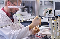 Eine Person mit Handschuhen und einem weißen Kittel führt ein Experiment durch.