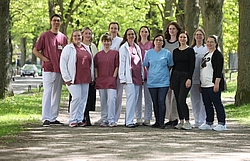 12 Personen sind auf einem Gruppenbild in einer hellen Allee zu sehen.