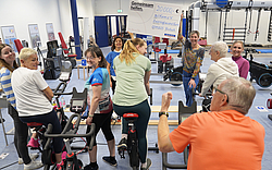 Eine Gruppe von Menschen freut sich, hält einen Spendenscheck hoch und benutzt teilweise Sportgeräte.