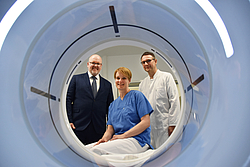 Drei Personen blicken durch eine CT-Röhre
