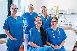 Vier Frauen und ein Mann in blauer Berufskleidung posieren in einem Behandlungszimmer.
