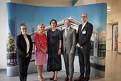 Fünf Personen in formeller Kleidung stehen vor einem großen Bild mit einem modernen Gebäude